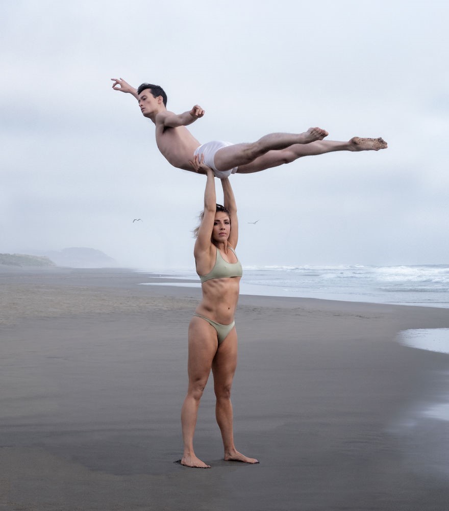 A girl holding a guy above her head on the beach.