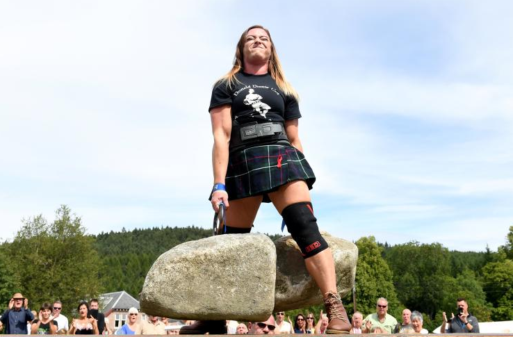 A girl lifting a boulder off the ground with one hand in front of a crowd.