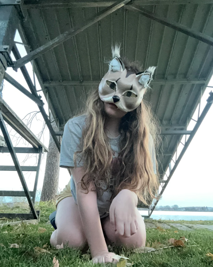 A young girl kneeling under a bridge with a wolf mask.